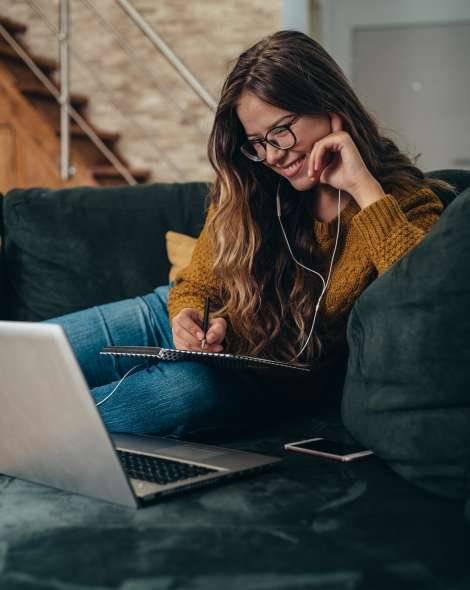 Young beautiful woman having online college class at home while using a laptop and headphones